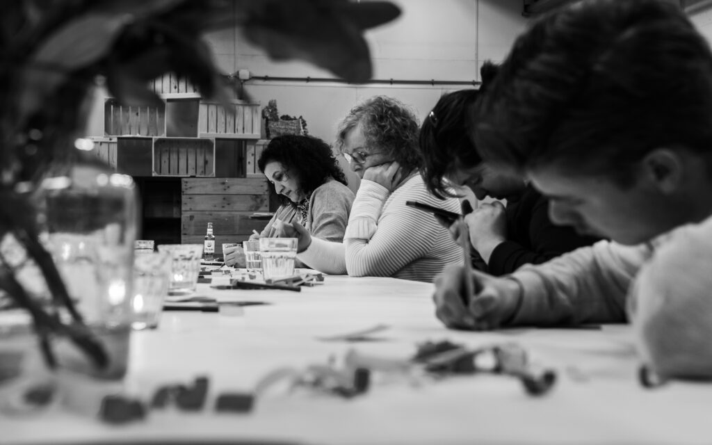 Deelnemers Manuela, Ida, Sanneke en Raf zitten naast elkaar aan tafel en vullen hun antwoorden op de vragen in op het vel.